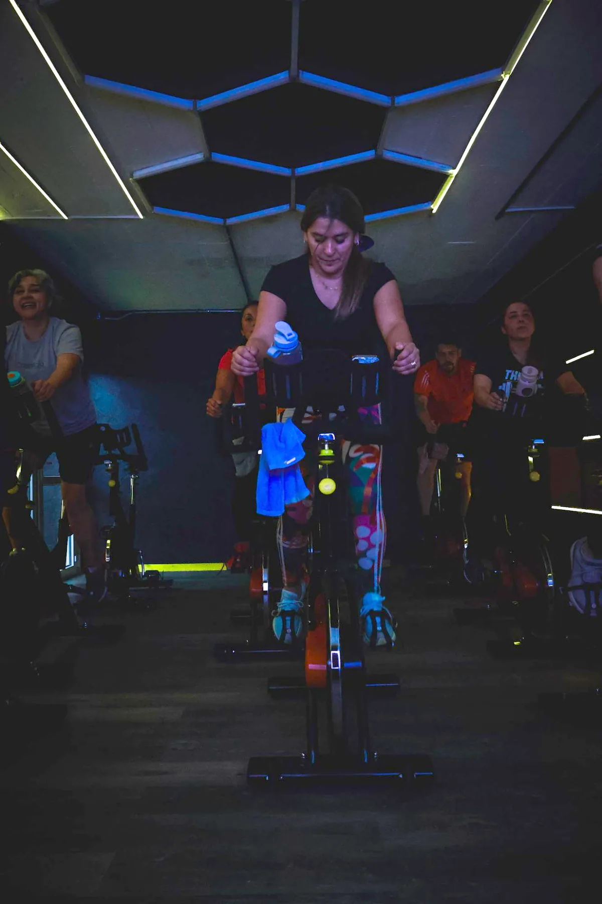 Alumna pedaleando en la sala de Indoor Cycling del Studio Aktiva-T, bajo el techo hexagonal con luces azules